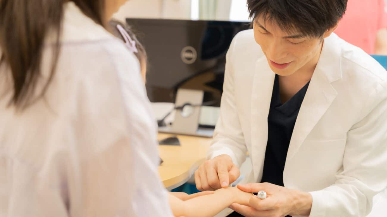 診察室で患者の手を確認する男性医師