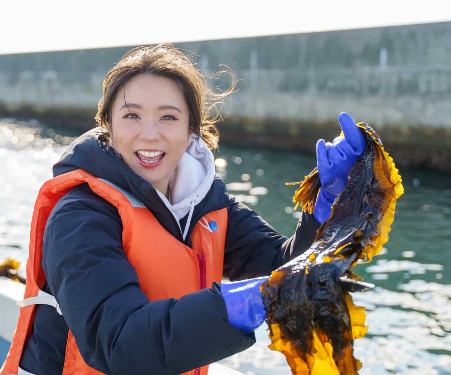 塩釜漁港の船上で、収穫したワカメを手に笑顔を見せる女性