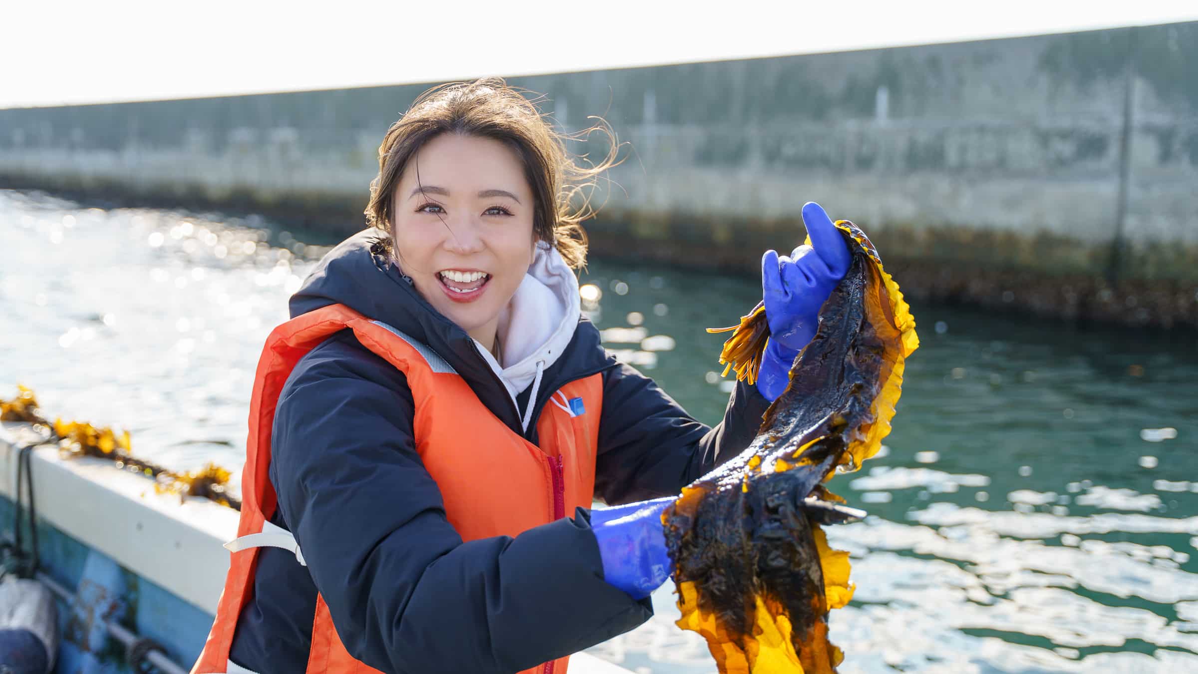 塩釜漁港の船上で、収穫したワカメを手に笑顔を見せる女性